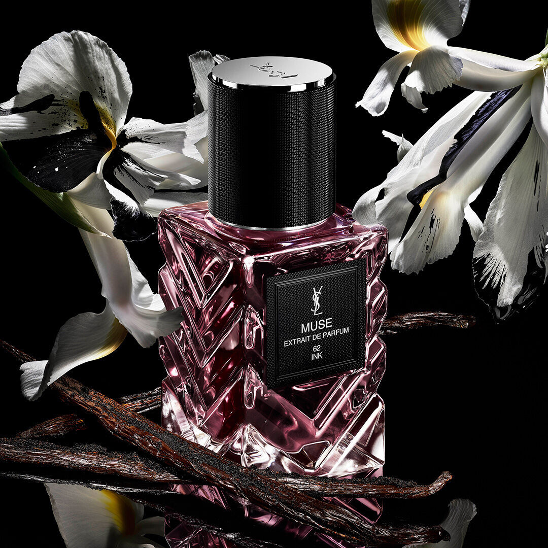 YSL Muse extrait de parfum bottle with white flowers and vanilla pods on black background.