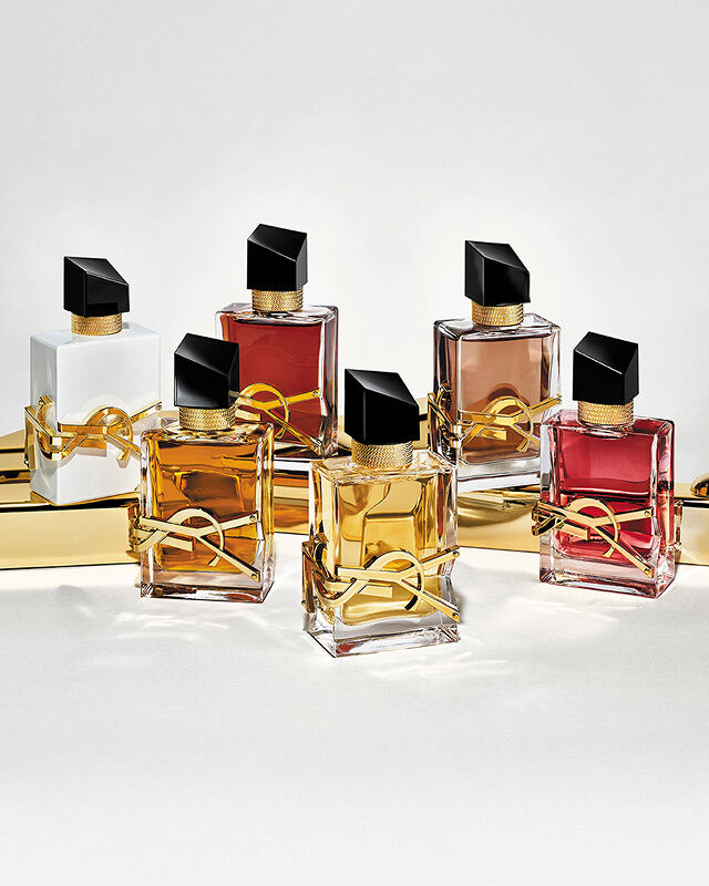 Group of Libre perfume bottles including L’Eau Nue Alcohol-Free, Eau de Parfum, Flowers & Flames, Berry Crush, and Eau de Parfum Intense, arranged on a reflective gold surface.