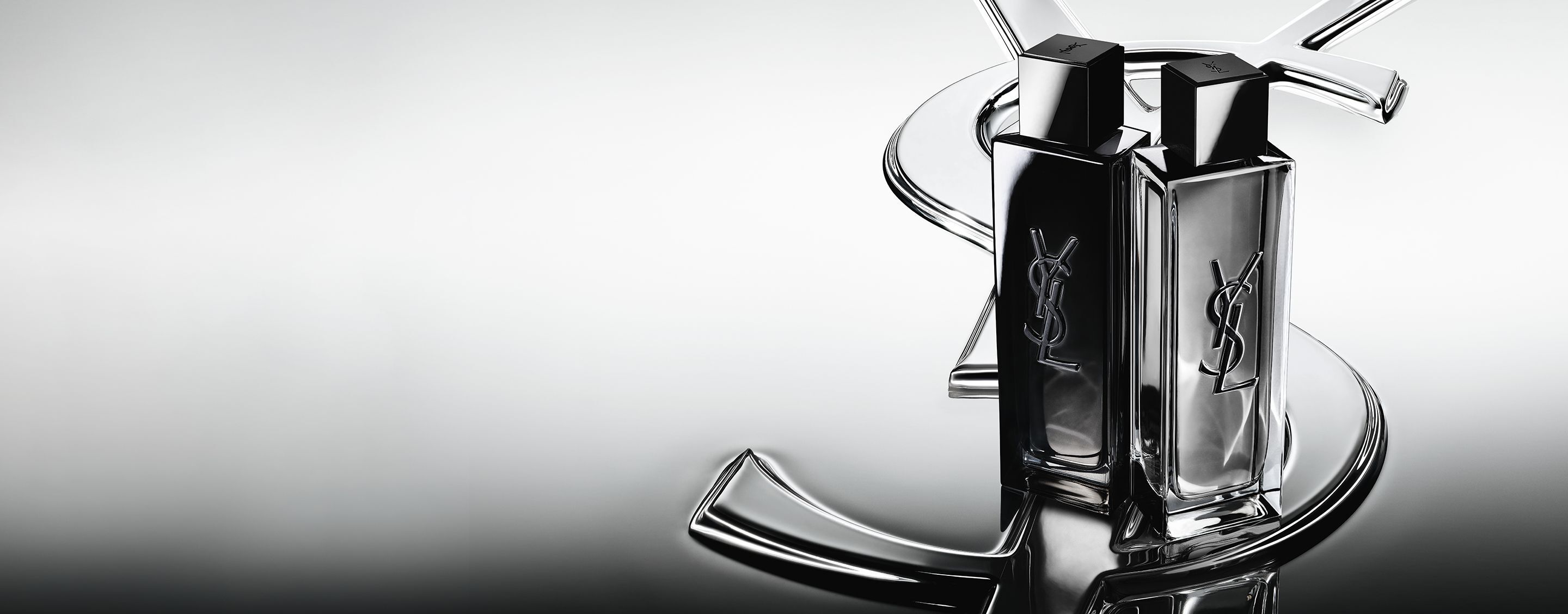 MYSLF Eau de Parfum and MYSLF Eau de Toilette Intense bottles standing side-by-side on a large YSL Cassandre logo with a reflective mirror effect.