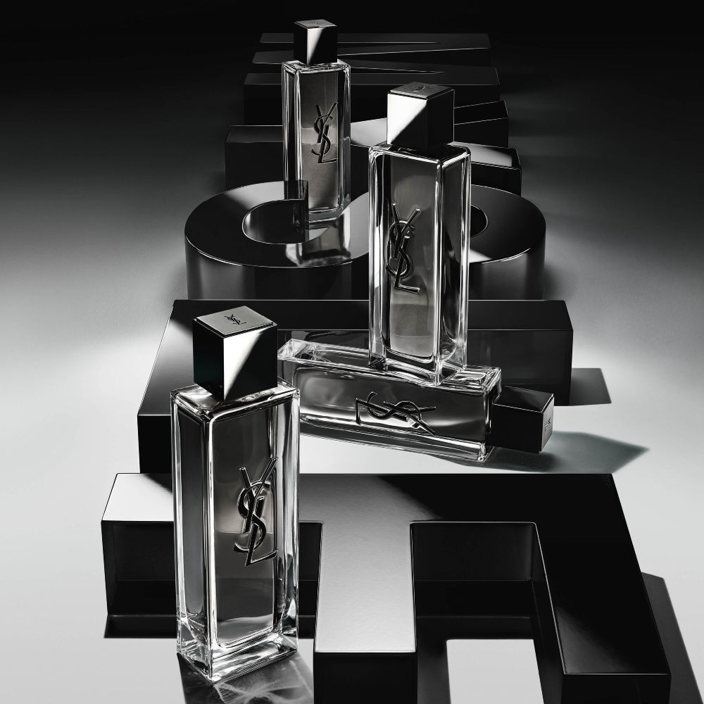 High-angle view of MYSLF Eau de Toilette Intense bottles arranged on large black 3D letters spelling MYSLF laid flat on the ground.