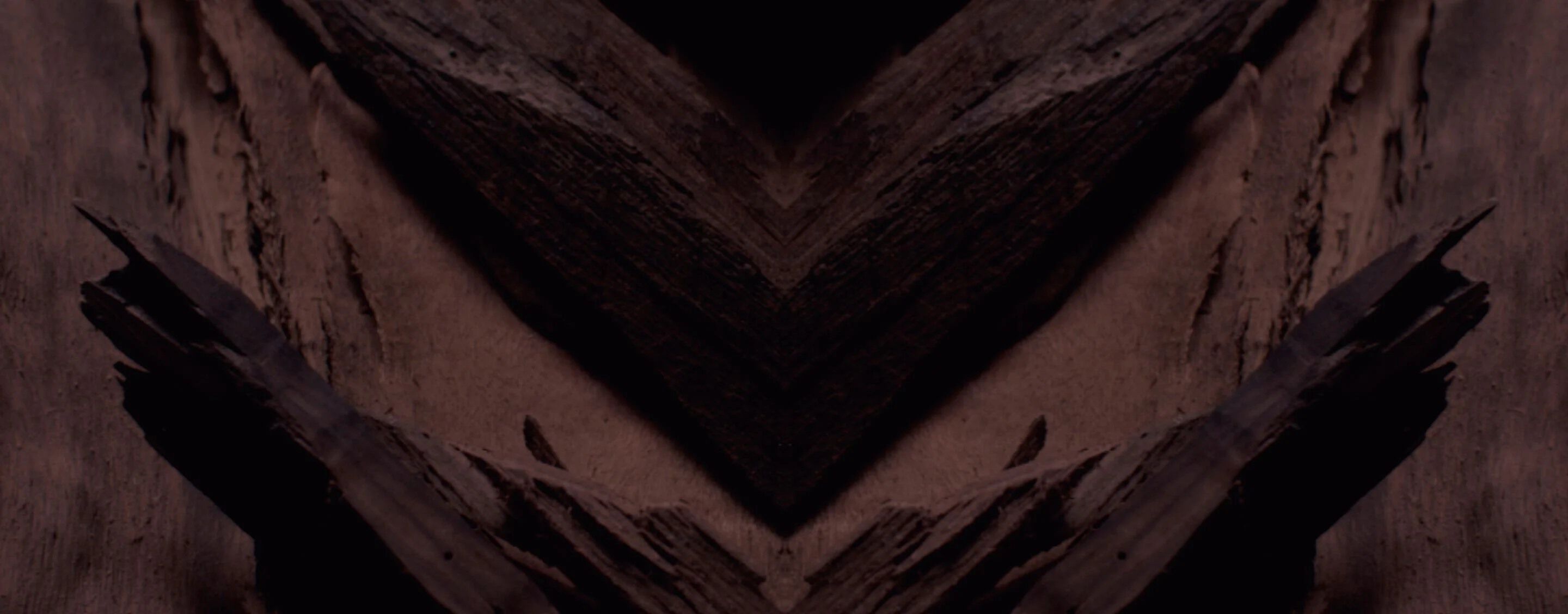 Dark, textured background with a prominent chevron pattern in
deep browns and blacks, designed for YSL LVP Extrait de Parfum
product display.